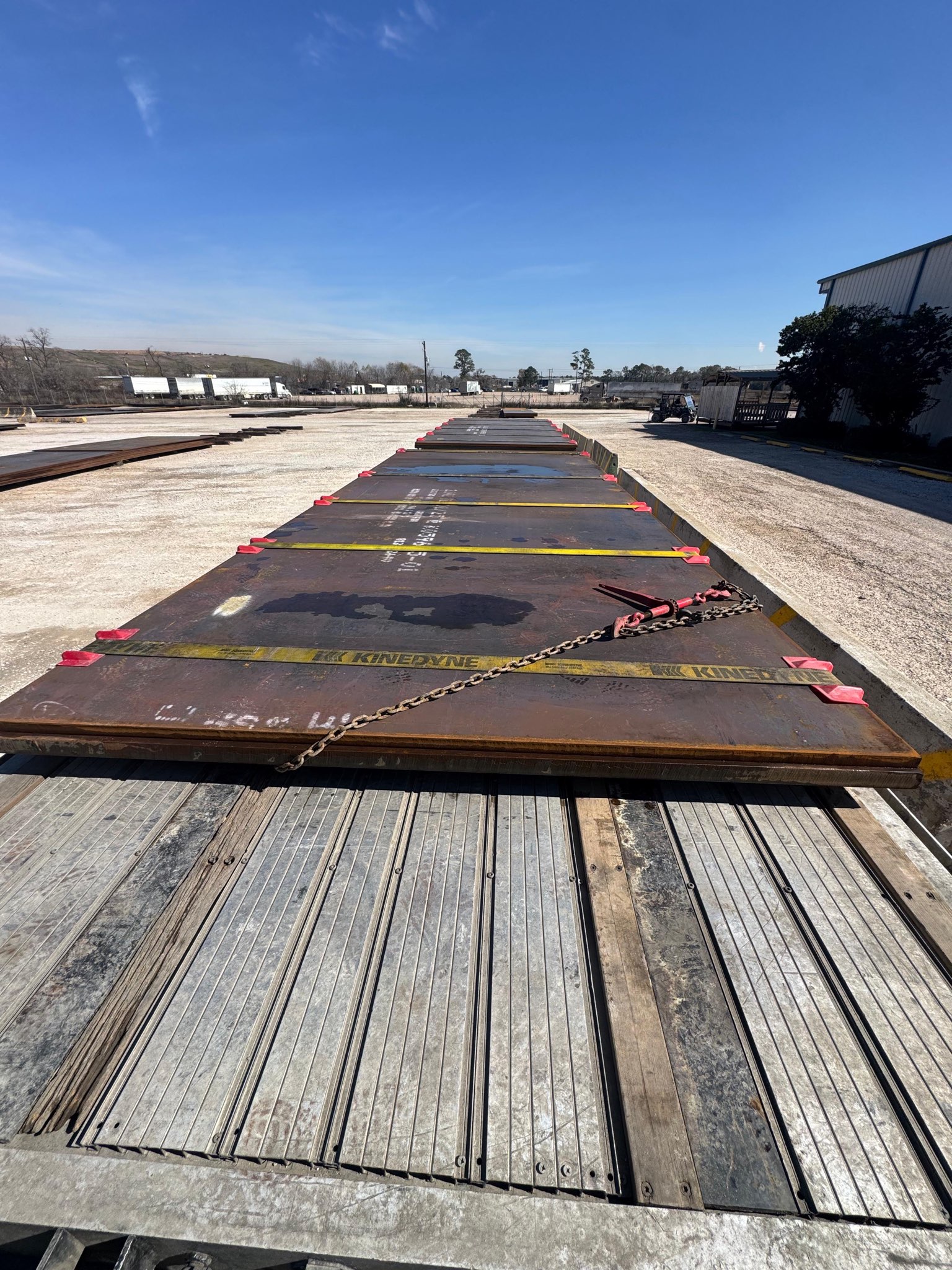 Steel plates chained and secured on a flatbed trailer viewed from deck level at a Houston freight yard