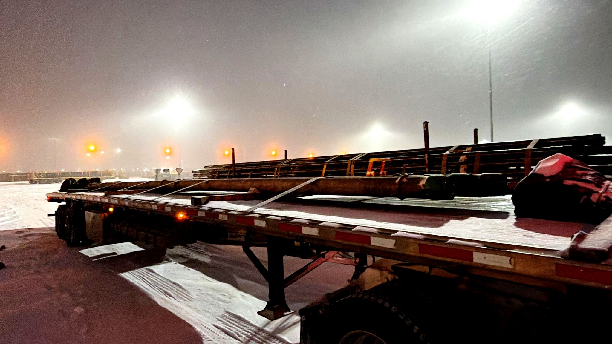Flatbed trailer loaded with pipe freight staged at night during Edmonton winter operations