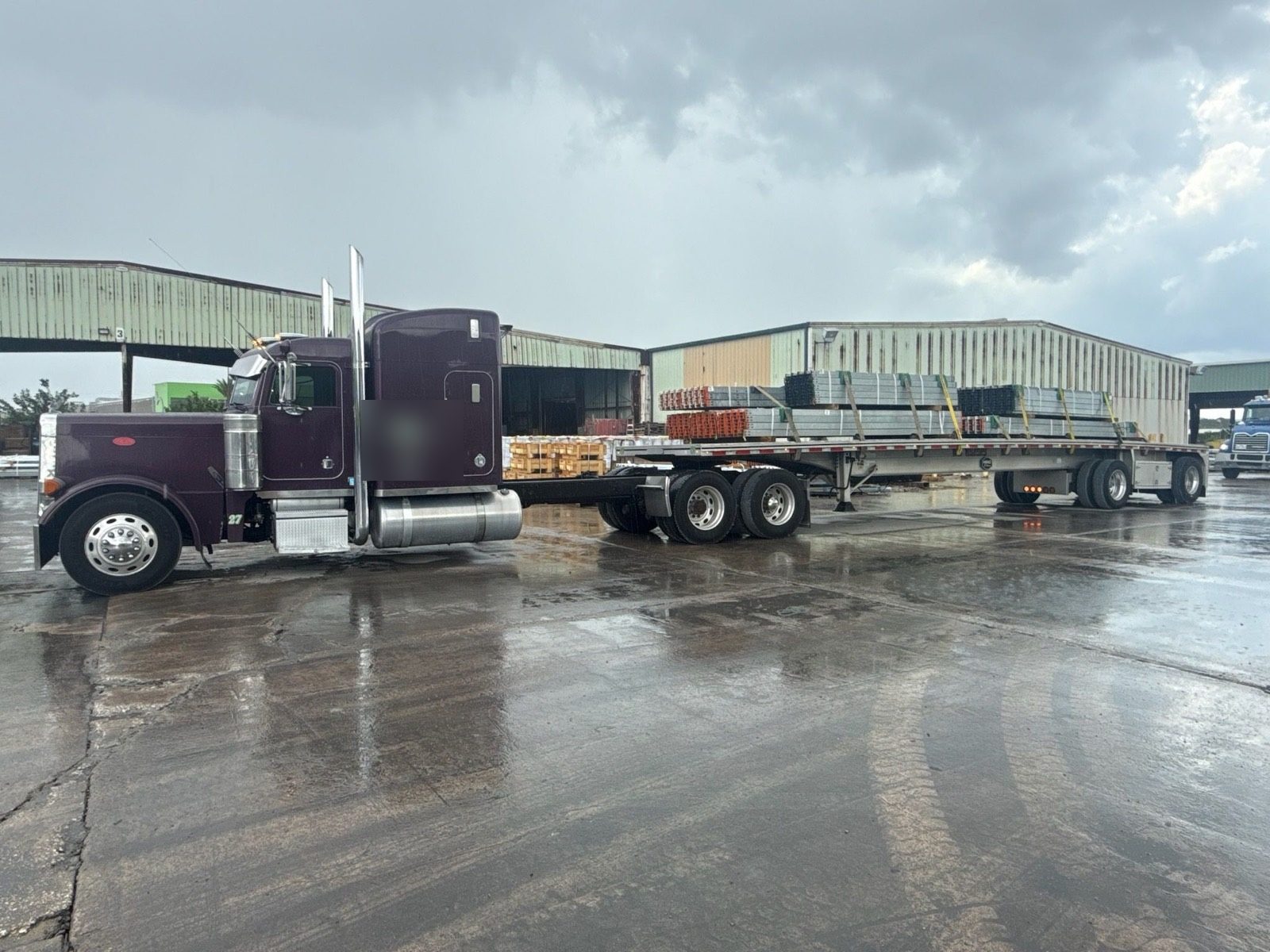 Flatbed of galvanized steel staged at a yard in the rain
