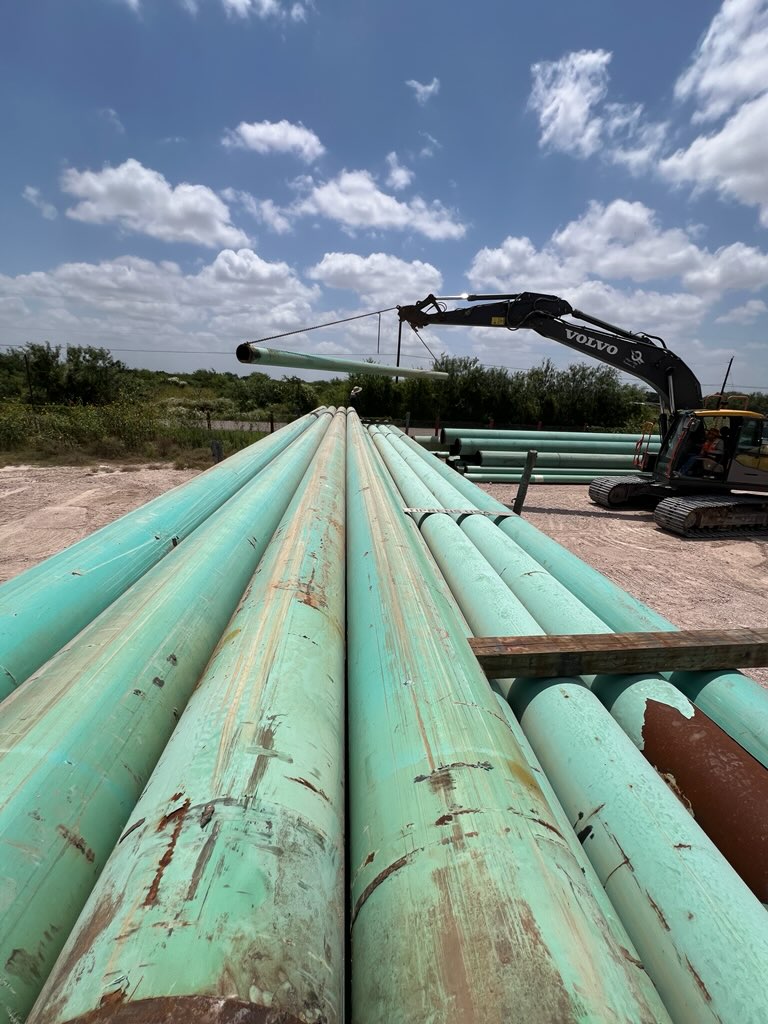 Looking down a flatbed deck loaded with OCTG pipe sections secured with yellow straps at a Houston industrial yard